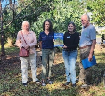 A group of people standing in a park holding a bookDescription automatically generated